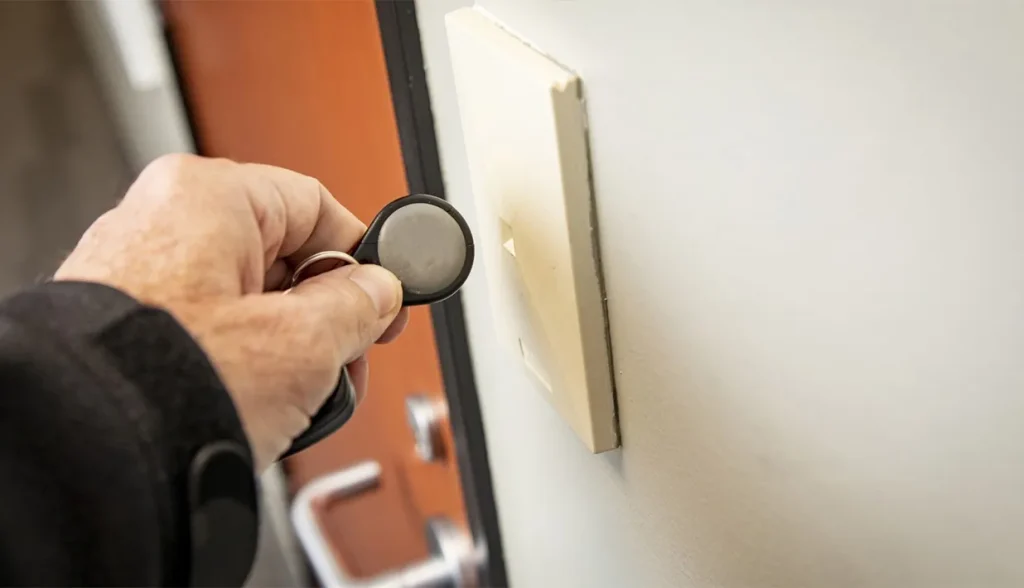 Mano sosteniendo un llavero RFID cerca de un lector montado en la pared, mostrando el proceso de comunicación.