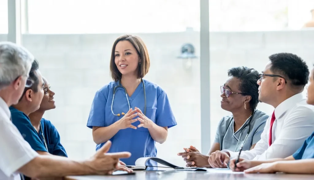 Healthcare professionals in a conference room, listening to a nurse-led discussion.