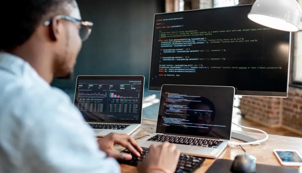 A software developer works at a desk with multiple screens displaying code, representing secure programming practices for NFC tag connection systems.