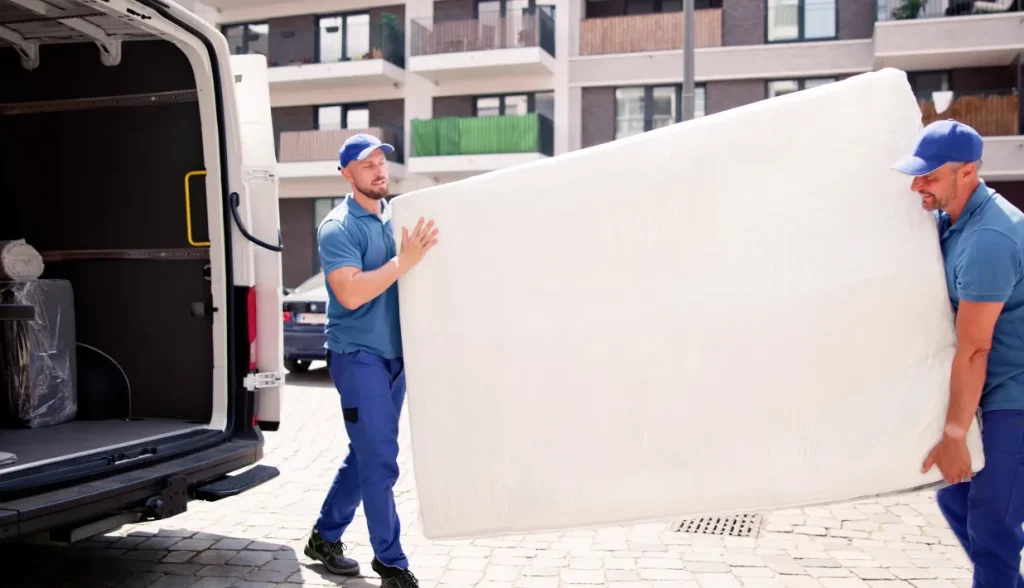 Two delivery workers carrying wrapped mattress for RFID mattress tracking shipment to hotel clients.