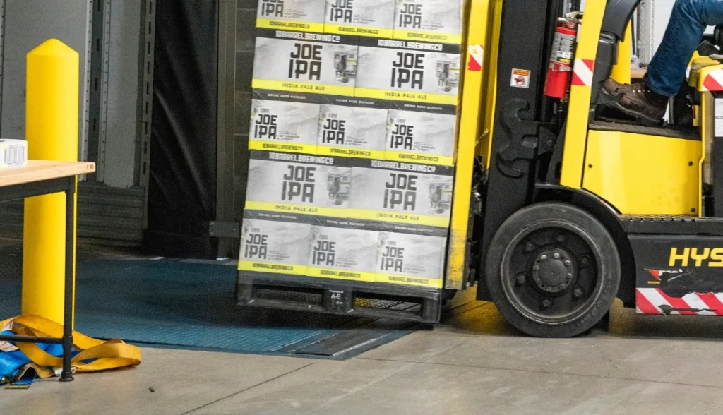 Yellow industrial forklift transporting stacked cases loaded on wooden pallet, warehouse material handling using RFID pallet tracking technology.