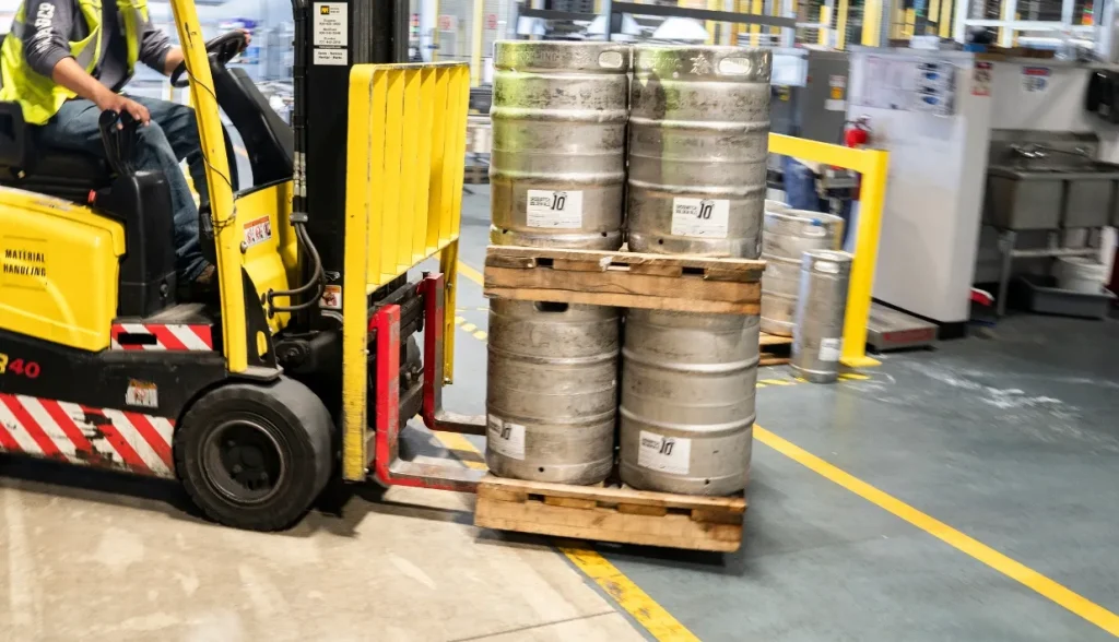 Warehouse forklift lifting wooden pallet stacked with metal kegs, industrial pallet handling monitored with RFID pallet tracking tags.