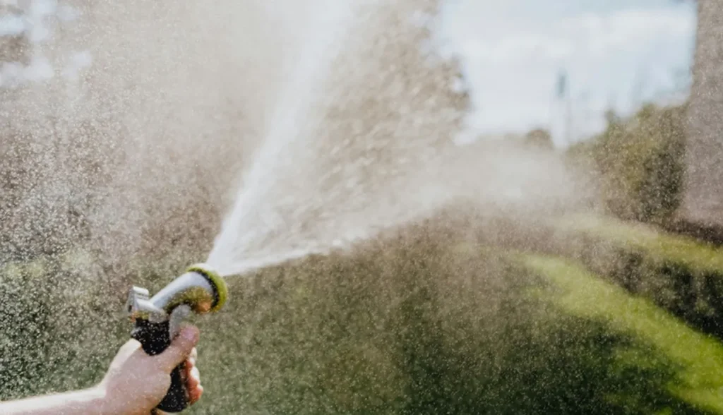 High‑pressure water spray shooting from a garden nozzle to simulate hot‑washdown cleaning for IP69 rated industrial RFID tags.