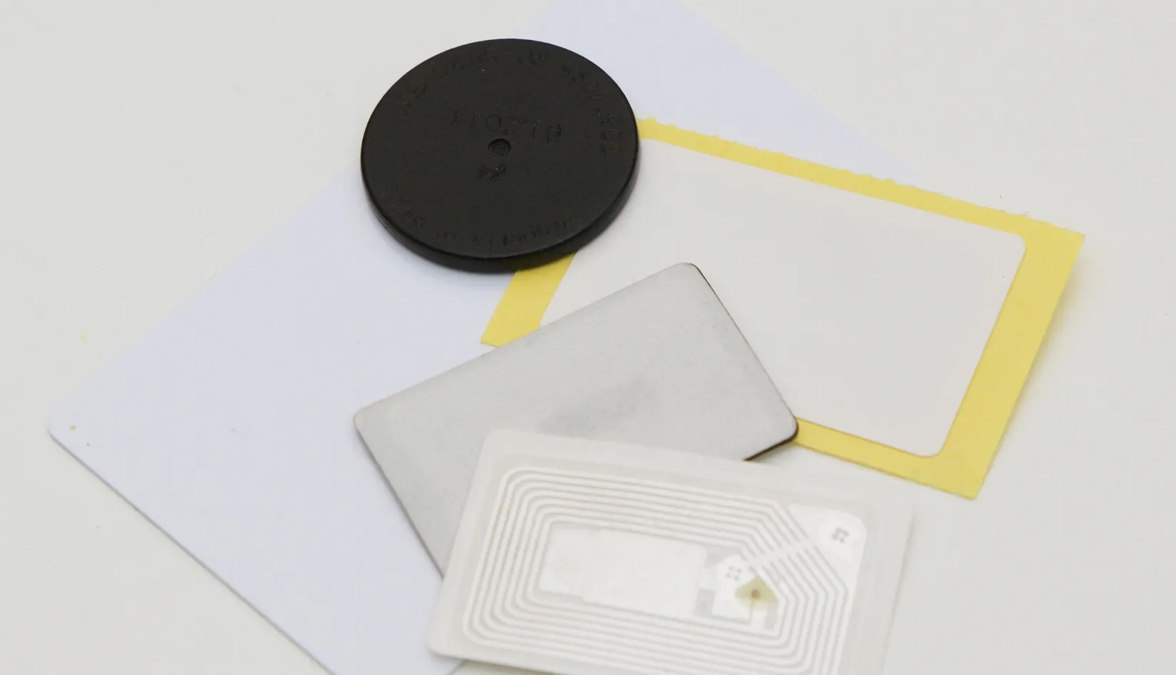 RFID Tag Materials How to Choose the Right Material for Your Application Assorted RFID tag materials including hard circular anti‑metal tag, metal‑resistant sticker tags, NFC inlay and blank adhesive labels on white background.