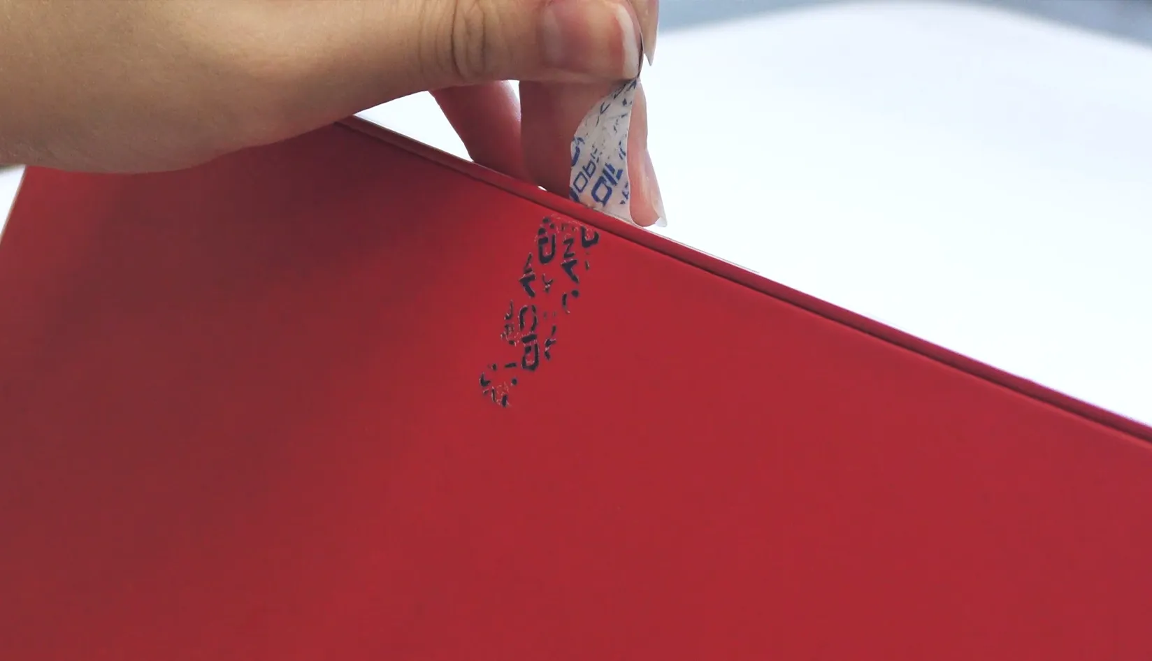 Tamper Proof Tag Guide Choosing the Right RFID Tag for Your Application Hand peeling a tamper-evident security sticker off a red box, showing visible residue left after removal, tamper proof RFID label anti-tampering demonstration.