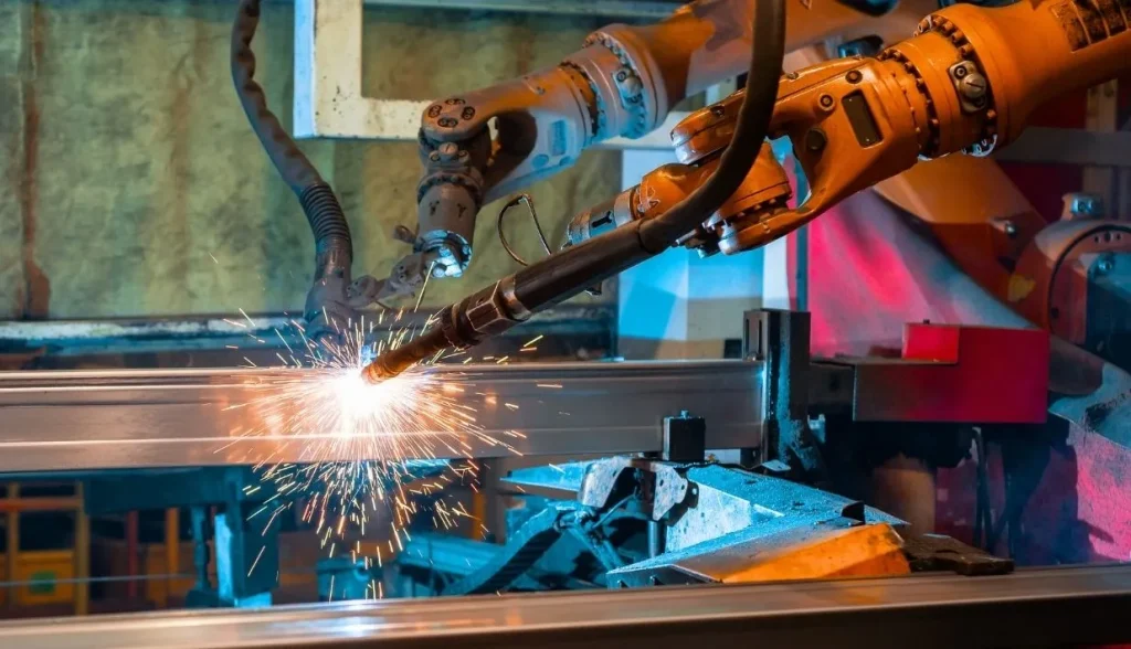Robotic welding station with hot sparks in heavy manufacturing, showing extreme high‑heat industrial conditions.